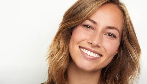 Woman with wavy brown hair smiling directly at camera against white background.