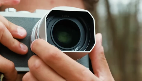 Close-up of hands holding a white compact camera with a dark lens element visible.