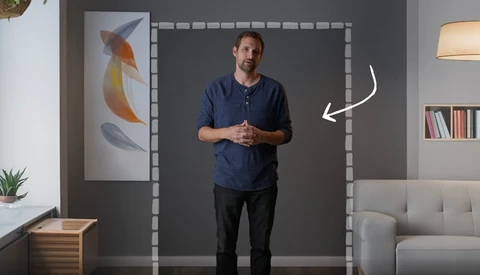 Man in navy shirt standing in front of a gray wall with taped frame outline and white arrow pointing right.