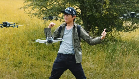 Drone operator in a grassy field wearing a cap and jacket, launching multiple drones.