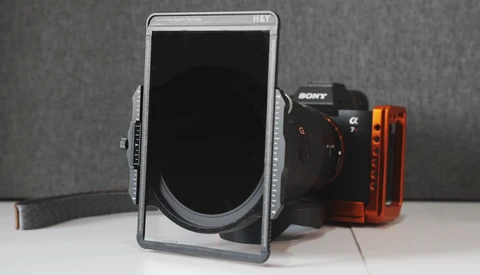Smartphone mounted in a rig holder with a Sony mirrorless camera and red LED light panel on a white surface.