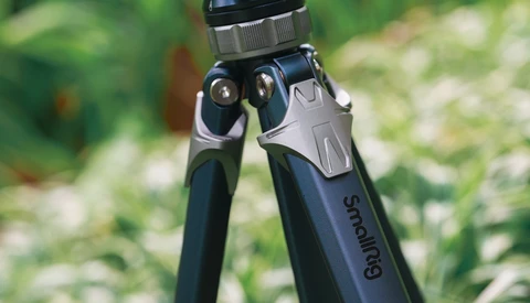 Close-up of a tripod head with ball joint and adjustment knobs against a blurred green outdoor background.