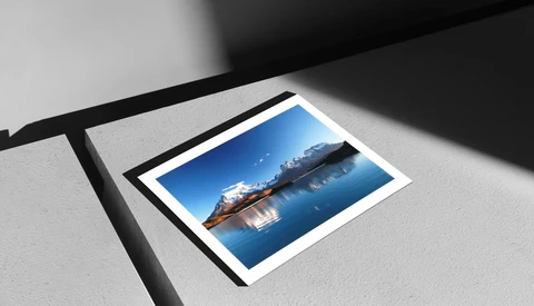 Polaroid-style photograph of a cargo ship on calm blue ocean water displayed on white surface with dramatic shadow.