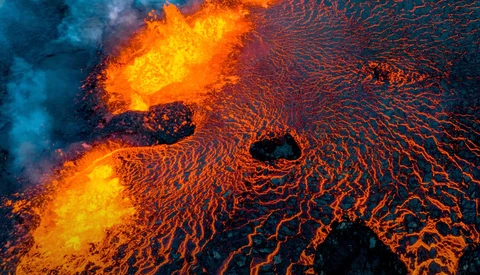 Aerial view of flowing lava with bright yellow-orange incandescent cores and darker solidifying edges creating intricate branching patterns.