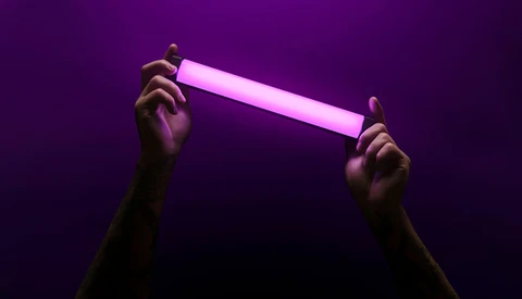 Two hands holding a glowing pink neon tube against a deep purple background.