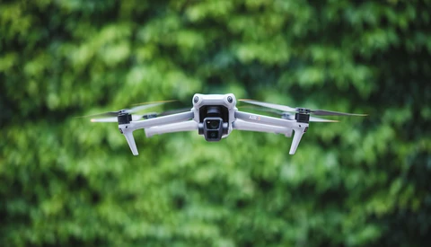 Compact quadcopter drone hovering against blurred green foliage background.