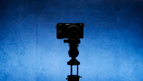 Sony mirrorless camera mounted on a tripod against a deep blue textured background.