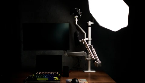 Professional studio setup with monitor, articulating desk lamp, and softbox lighting on dark background.