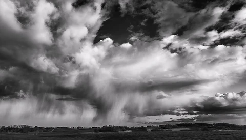 Dramatic black and white storm clouds with rain curtains over a flat landscape.