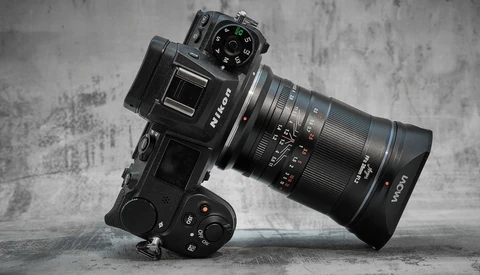 Mirrorless camera with telephoto lens mounted on motorized gimbal head against textured gray backdrop.