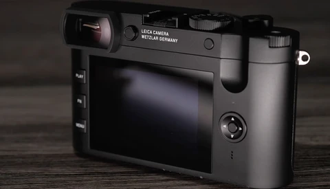Leica camera with rear LCD screen displayed at three-quarter angle on wooden surface.