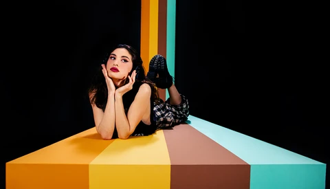 Woman resting her head on a colorful geometric surface against a black background.