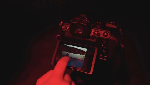 Photographer's hand holding a mirrorless camera with LCD screen visible in red-tinted lighting.