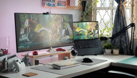 Dual-monitor creative workstation with laptop displaying landscape scene and desktop displaying forest environment.