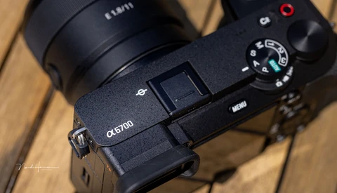 Sony α5700 mirrorless camera with attached lens on wooden surface, showing top plate controls and mode dial.