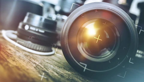 Camera lens with golden light flare and optical elements visible through glass.