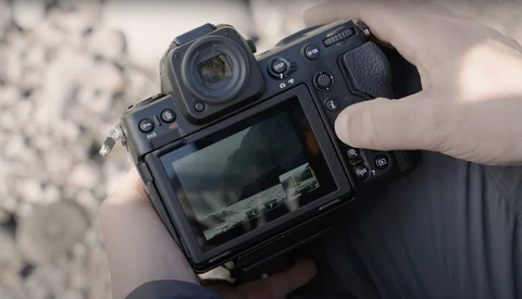 Mirrorless camera held in hands displaying landscape scene on rear LCD screen.