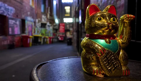 Golden beckoning cat figurine with red ears and green bib on a blurred nighttime street.