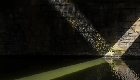 Sunlight streaming through a narrow passageway between dark stone walls and still green water below.