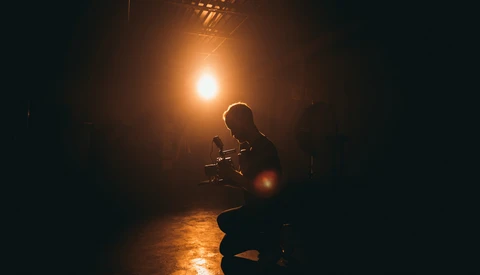 Silhouetted figure holding a camera in a dark corridor, backlit by warm golden light.