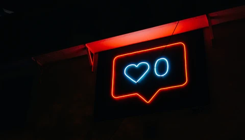 Neon sign displaying a heart outline and zero, glowing blue and red against dark background.