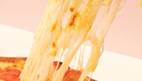 Melted cheese stretching from a pizza slice against a soft pink background.