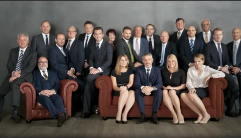 Professional group portrait of approximately 20 business professionals in formal attire arranged in three rows.