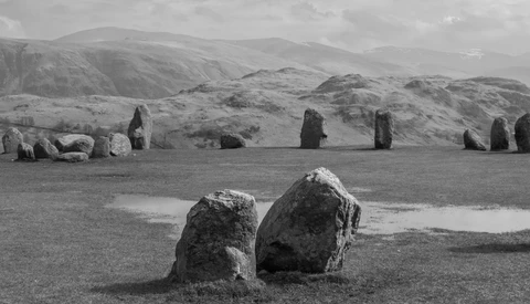 Two weathered standing stones in foreground with row of distant megaliths and rolling hills in black and white.