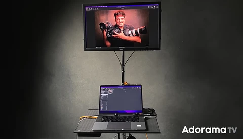 Monitor on adjustable stand displaying portrait of person with arms outstretched, laptop below showing editing interface.