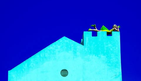 Minimalist architectural photograph of a bright cyan building with geometric forms against a deep blue sky.