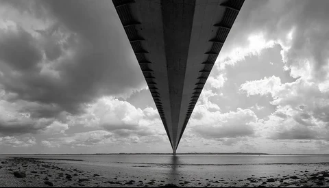 Long bridge viewed from underneath, stretching toward horizon with dramatic cloudy sky.