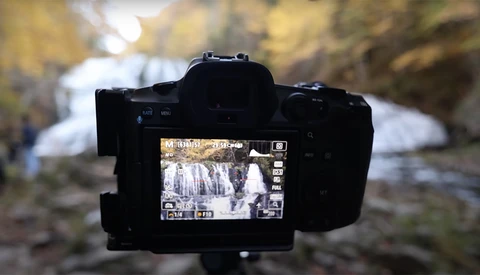 Camera on tripod displaying waterfall footage on LCD screen with blurred background.