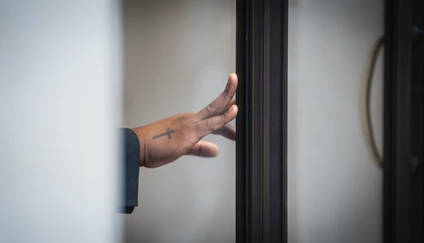 Hand reaching through a dark doorframe against white walls, fingers extended in an open gesture.