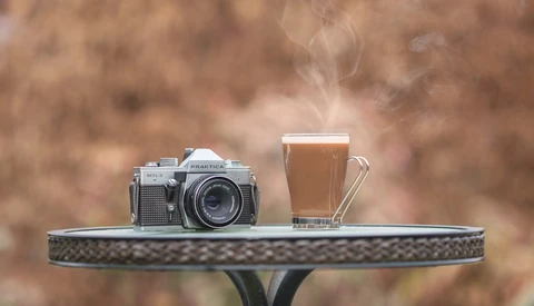 Vintage rangefinder camera and glass of beer on decorative table with blurred brown background.