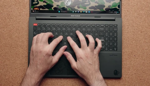 Overhead view of hands typing on an ASUS Vivobook laptop with camouflage pattern on screen.