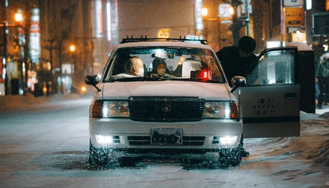 Taxi cab driving through flooded urban street at night with city lights in background.