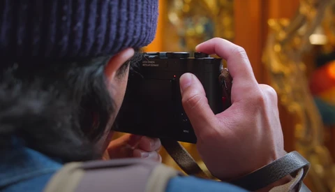 Photographer's hands holding a compact camera in portrait orientation outdoors during golden hour.