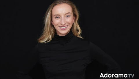 Woman with blonde wavy hair smiling at camera wearing black turtleneck.