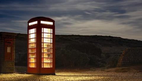 Illuminated red British telephone box standing alone in a rocky desert landscape at dusk.