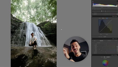 Man crouching on rocks beside a waterfall in a forested ravine.