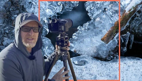Photographer in winter gear holding a camera on a tripod amid ice-covered rocks and frozen surfaces.
