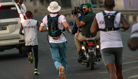 Urban street runners moving past a motorcyclist during daytime in a busy city setting.