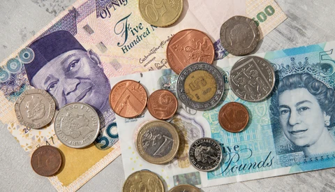 British banknotes and coins arranged on a white surface, including a £5 note and £10 note with various denominations of coins.