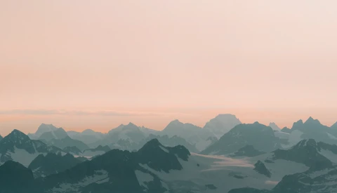 Layered mountain silhouettes in mist under a peachy dawn sky.