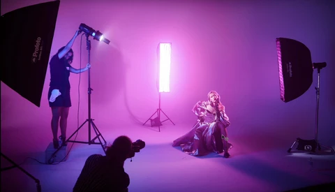Professional studio photography shoot with magenta-pink lighting and multiple light sources positioning a seated subject.