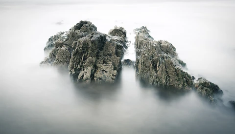Two jagged rock peaks emerging from dense fog and mist in a mountainous landscape.