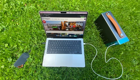 Laptop displaying a video streaming interface with an external hard drive connected via USB cable on grass.