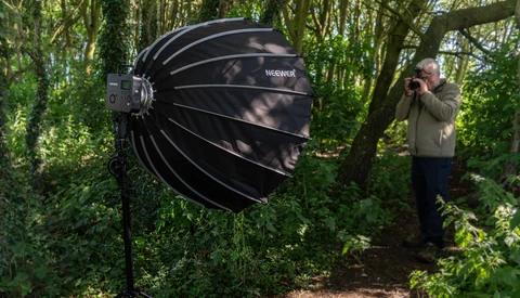 Large black parabolic softbox suspended in a forest setting during outdoor photography shoot.