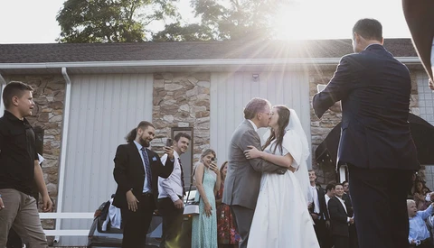 Bride and groom kissing during outdoor wedding ceremony with guests watching.