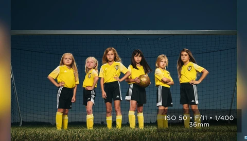 Six young soccer players in yellow jerseys and black shorts stand in a line in front of a goal net.